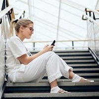 Foto av en kvinna som sitter i en trapp i v&aring;rdkl&auml;der med en telefon som hon tittar p&aring;.